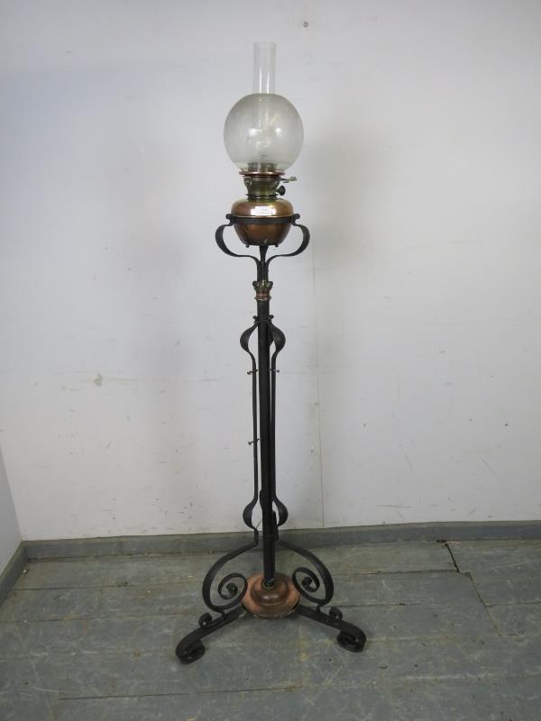 An Art Nouveau floor-standing wrought iron and copper oil lamp, on scrolled tripod supports.