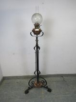 An Art Nouveau floor-standing wrought iron and copper oil lamp, on scrolled tripod supports.