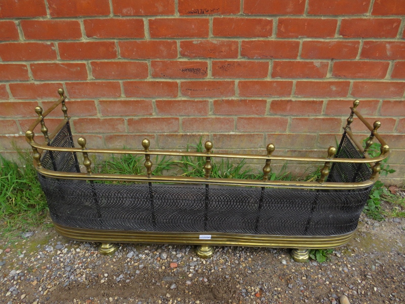 An Edwardian brass and wire mesh fire fender, the ball finials above turned brass spindles, with