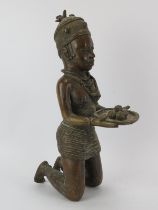 Tribal Art: An African Benin style cast bronze kneeling figure offering cocoa beans. 46.5 cm height.