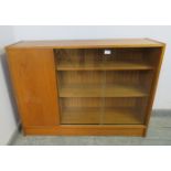 A mid-century teak low enclosed bookcase, having sliding glass doors opening onto two loose shelves,