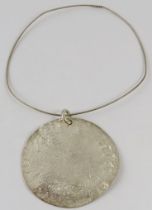 A large silver Artisanal disc pendant, 7.8cm diameter approx, on silver wire collar, with feature