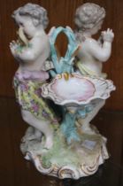 A Continental porcelain table centre piece, in the form of two putti, with scallop salts, factory ma
