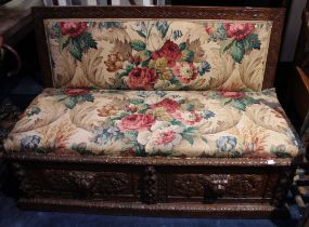 A carved oak bench with hinged upholstered seat revealing storage