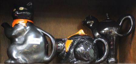 Three black cat ceramic teapots, one with arched back, two with orange bows about their necks (3)