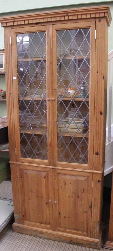 A pine display cabinet with two leaded doors over two cupboard doors