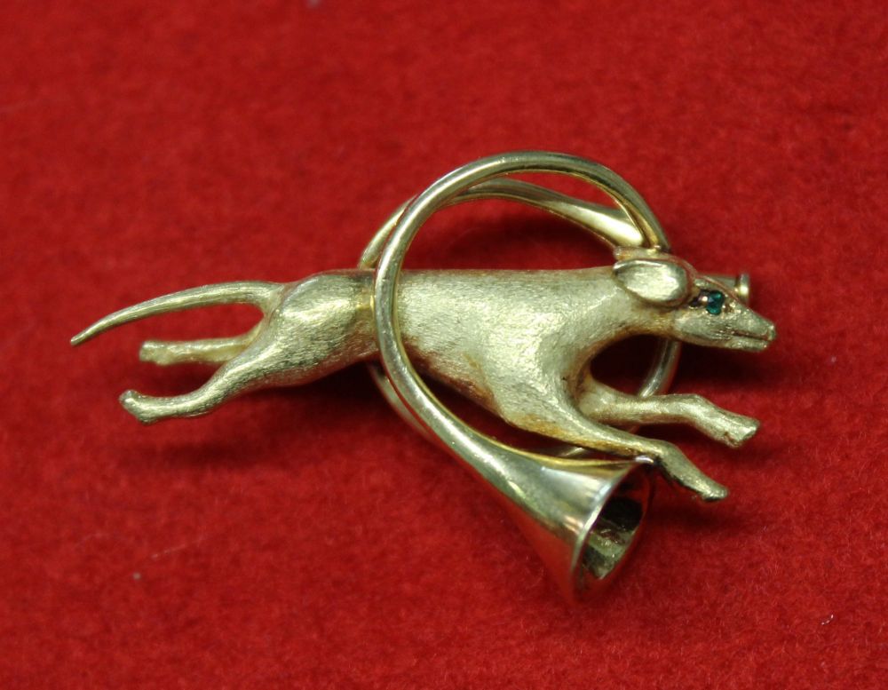 An 18k pin brooch, modelled as a running hound leaping through a French Hunting horn, hound set gree