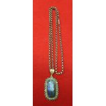 An Opal, set in a gold coloured frame mount, inset cut green stones, suspended from a 9ct gold chain