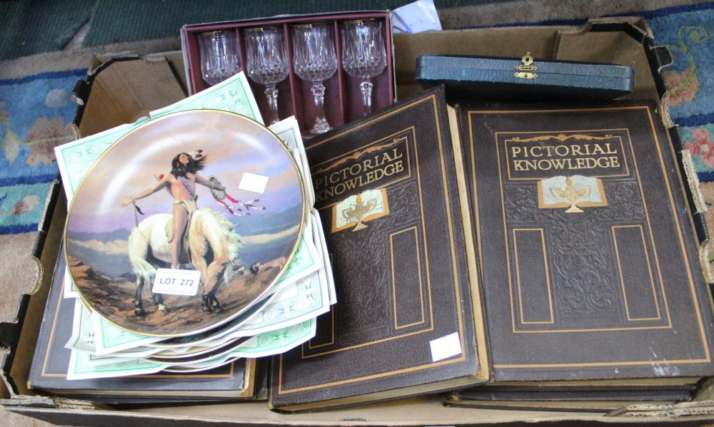 A box of assorted items includes books, glasses, collectors plates and tea knives