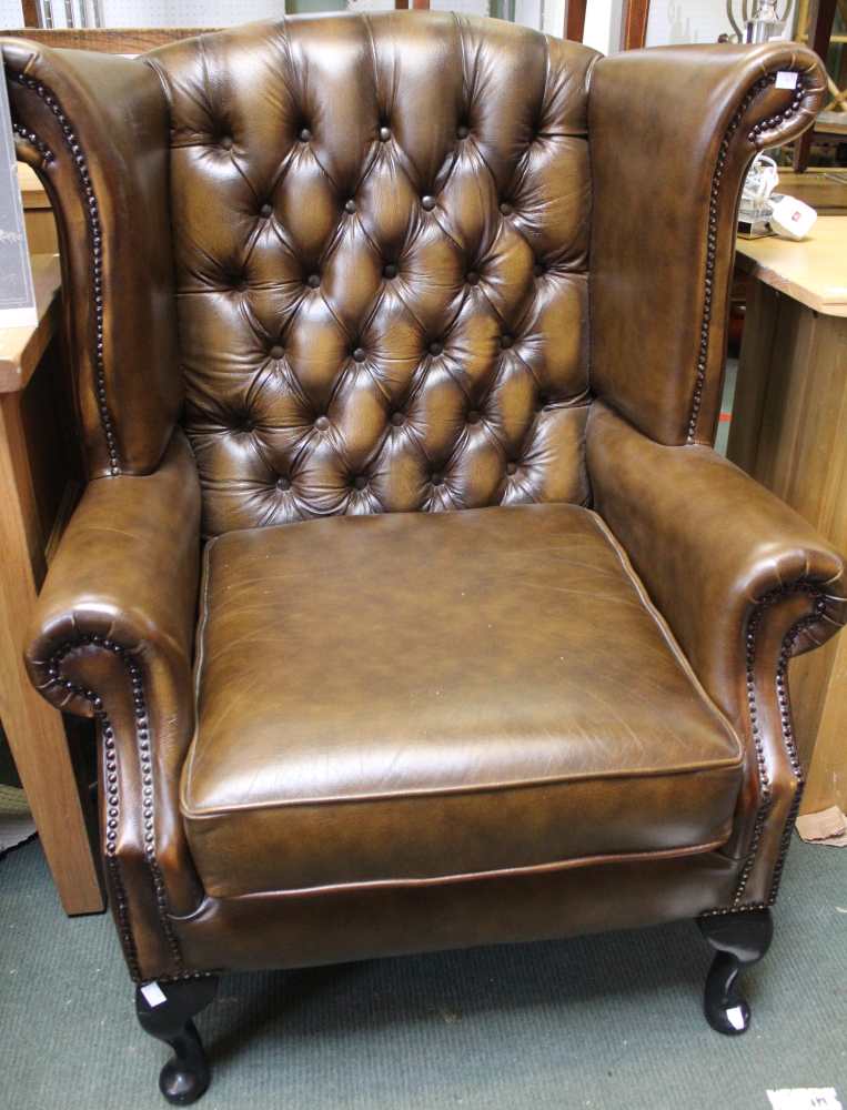 A brown leather wingback chesterfield style armchair