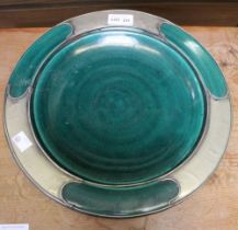 An Arts and Crafts design green glazed plate with pewter mounts, in a "Liberty" style 30cm diameter