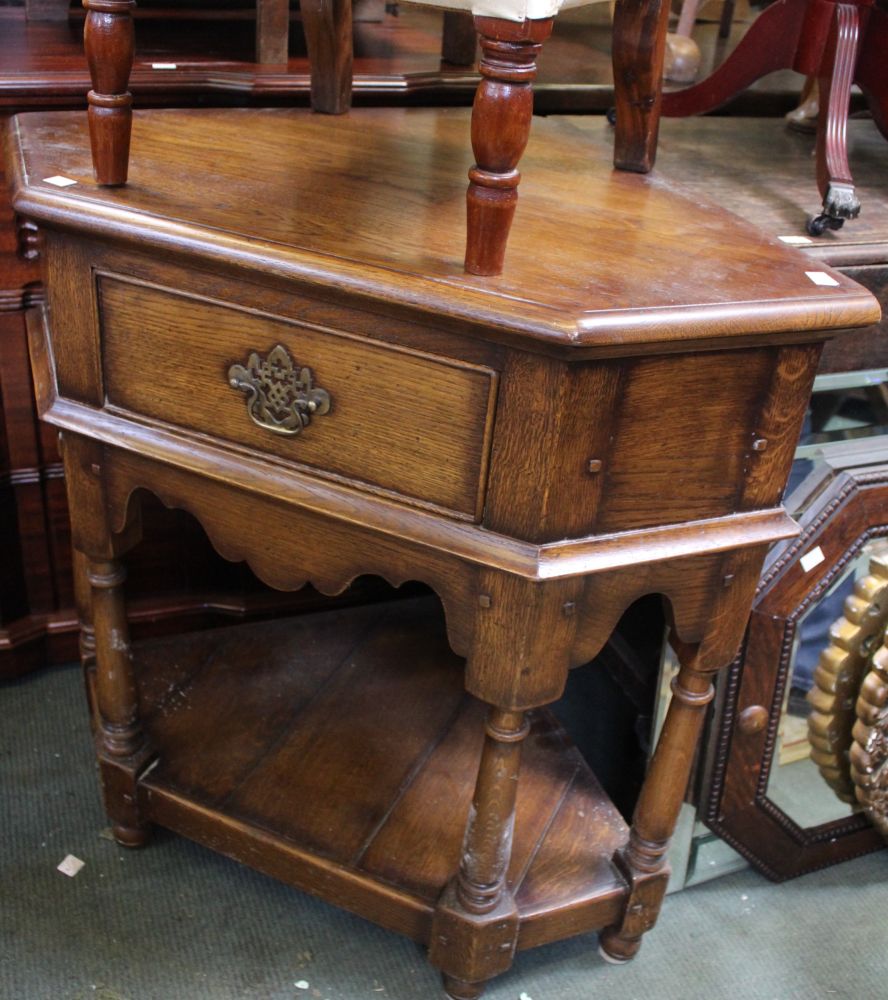 An oak corner table with single drawer and open under tier
