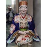 A Japanese ceramic figure, in kneeling contemplative pose, painted and gilded courtly robes, in the