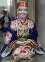 A Japanese ceramic figure, in kneeling contemplative pose, painted and gilded courtly robes, in the