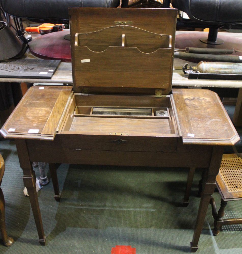 An early 20th century oak writing table with lift up lid and fold out writing slope