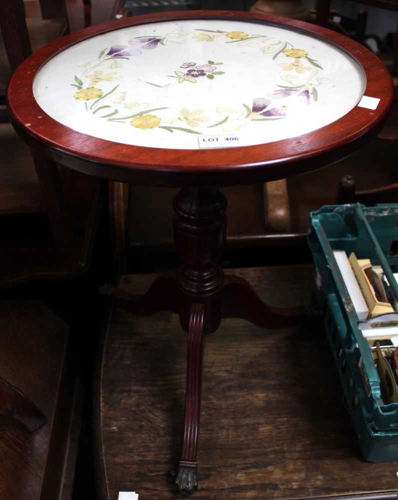 A low tripod wine table with claw caster feet and silk upholstered top beneath glass