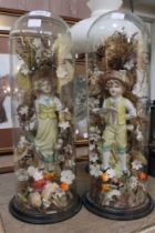 A pair of Victorian glass domes on wooden turned bases containing figurines of a boy and a girl