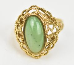 A yellow gold and jade dress ring, the central oval cabochon stone in a pierced rope twist