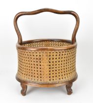 A French Belle Epoque period caned magazine holder, with shaped handle, above the oval basket with