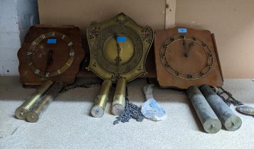 A group of three wall hanging pendulum clocks, each with two weights, and with two pendulums
