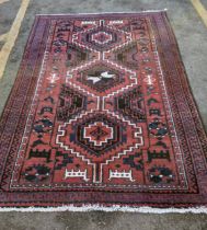 A handwoven Afghan rug with geometrical motifs on a dark red ground with triple guard border