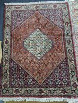 A Persian hand woven and floral patterned red ground rug, triple guard boarders and tasselled