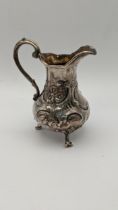 A silver three footed cream jug having floral embossed decoration 128.4g Location: