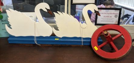A painted wooden fretwork model of two swans and a painted wheelbarrow wheel Location:
