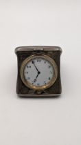An early 20th century silver cased travel clock engraved with inscription, having a white enamel