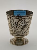 A silver drinking vessel decorated with an abstract design raised on a circular stepped pedestal