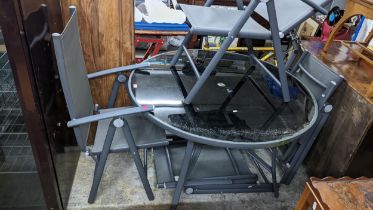 A glass topped and grey coloured metal and plastic garden table, inset circular black coloured glass