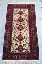 An Afghan Kazak hand woven rug having a beige centre with repeating motifs, surrounded by red