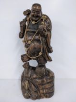 A Chinse treen carved figure of a smiling Buddha, holding a staff to one hand, 57.5h, Location: