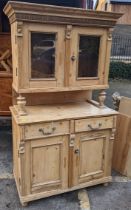 A pine, probably French, kitchen cupboard with a pair of glazed doors supported by two pillars