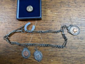 A silver watch chain with attached silver and gold fob metal, metal horse shoe charm, a football