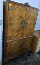 A walnut drinks cabinet, carved pediment over twin doors with brass hinges and escutcheons, over