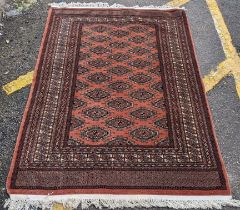 A Bokhara hand woven red ground rug having geometric designs and tasselled ends, 190cm x 126cm