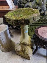 A weathered garden carved sandstone bird bath on a plain column, supported on four dolphin heads and