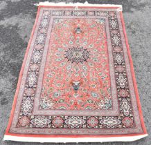 A Isfahan part silk rug with entwined flowering vine decoration on a salmon pink ground with a