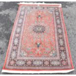 A Isfahan part silk rug with entwined flowering vine decoration on a salmon pink ground with a