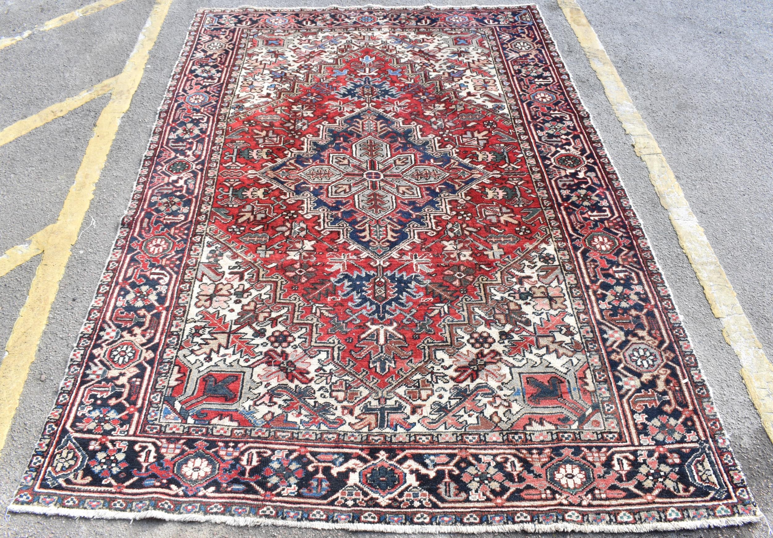 A Persian Heriz hand woven rug, having a red ground with a central motif within a field of