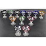 A set of twelve Bohemian coloured coupe glasses having flashed bowls upon faceted and lobed stems