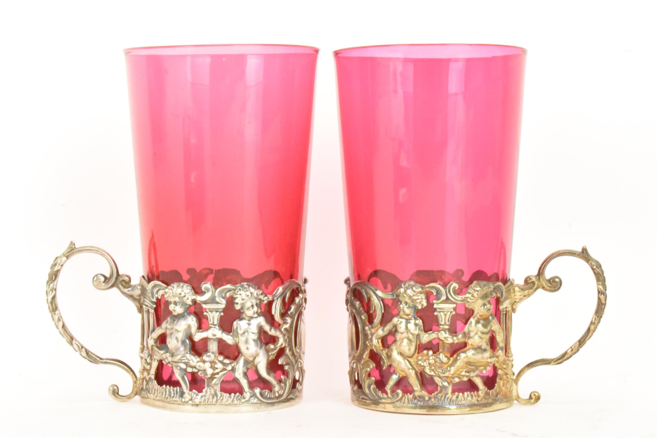 A pair of Edwardian silver glass holders with a pair of cranberry glasses, the holders ornately