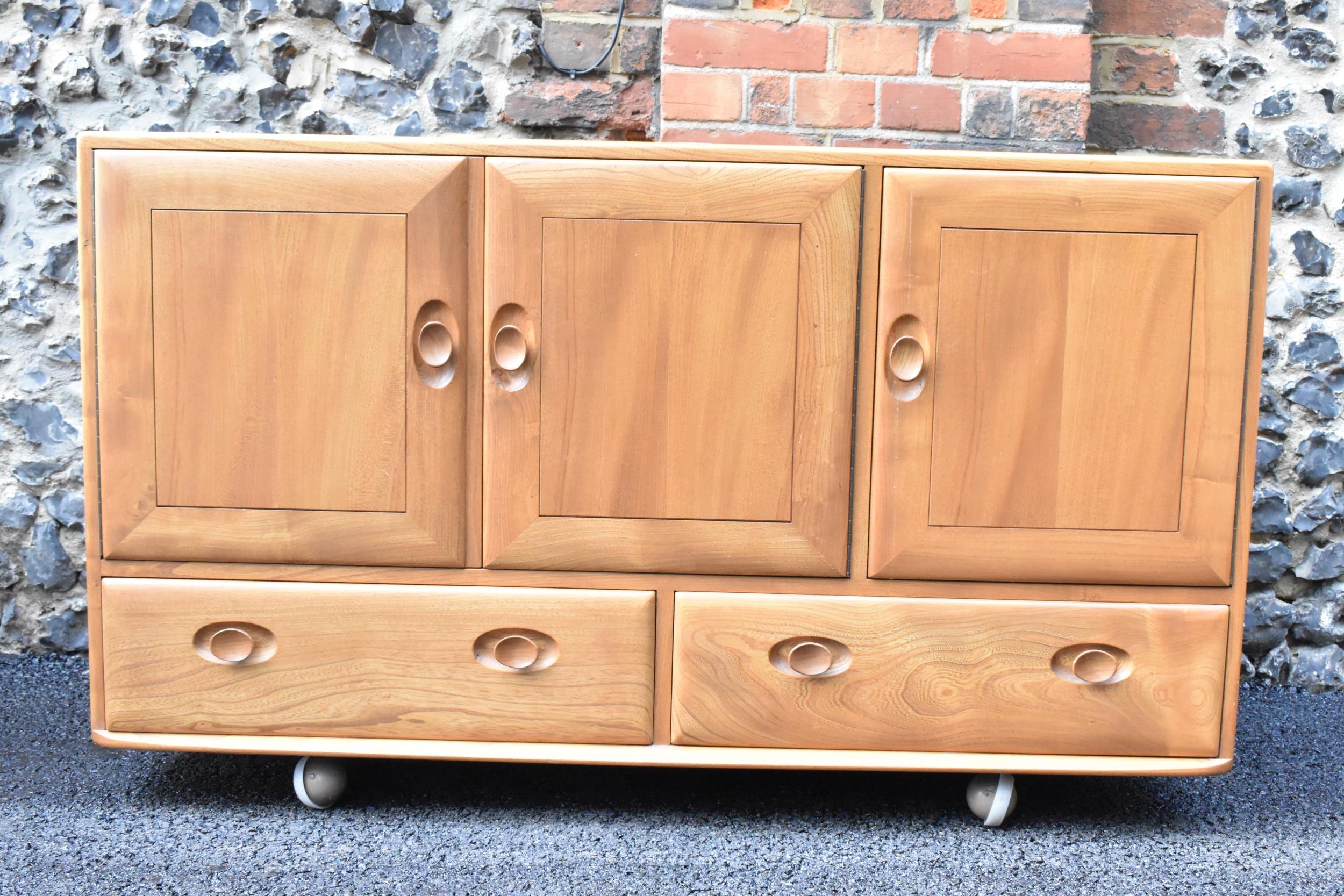 A mid 20th century Ercol Windsor range light elm sideboard, mode 468, having three cupboard doors