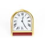 A Cartier travel alarm clock, having an arched top gilt metal case with red lacquer below, white