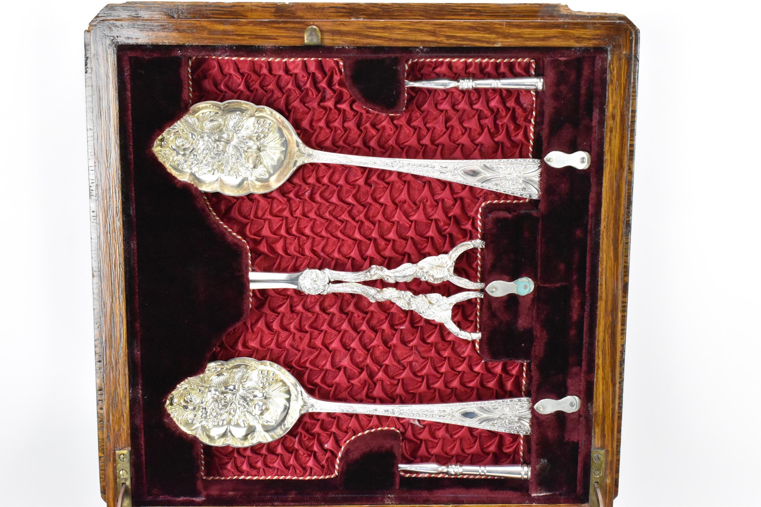 A late Victorian oak cased silver plated dessert canteen, consisting of two berry spoons, grape - Bild 5 aus 7