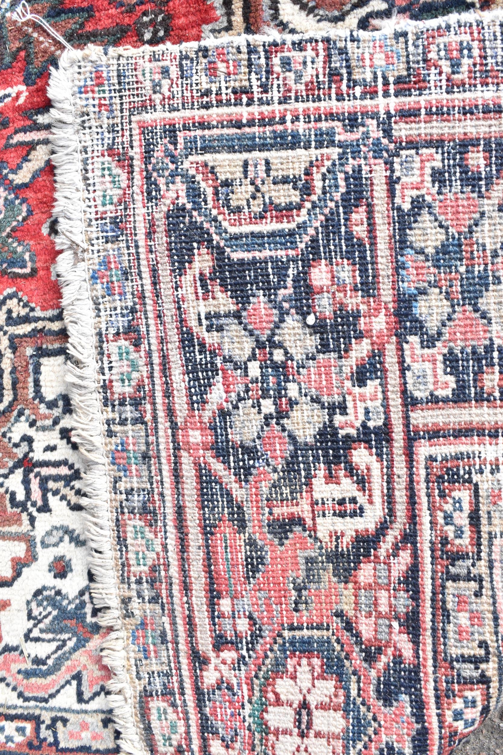 A Persian Heriz hand woven rug, having a red ground with a central motif within a field of - Image 8 of 8