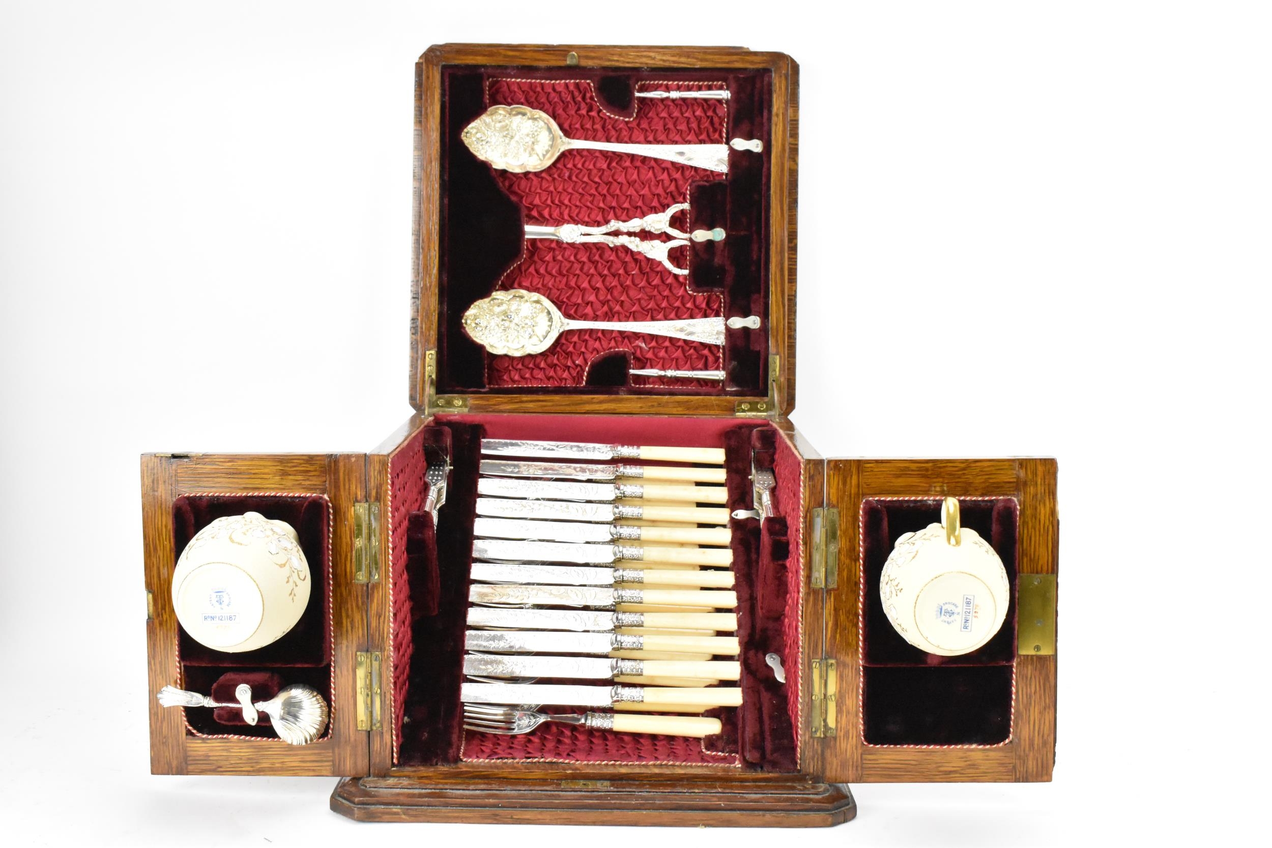 A late Victorian oak cased silver plated dessert canteen, consisting of two berry spoons, grape