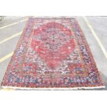 A Persian Heriz hand woven rug, having a red ground with a central motif within a field of