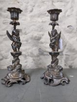 A pair of Victorian silver plated candlesticks, seated winged putti standing on entwined dolphin